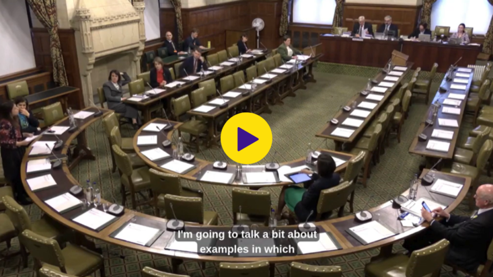 Screengrab of a video clip set at Westminster. There are long, curved tables and a handful of people sat at the table. There is a play icon in the middle.