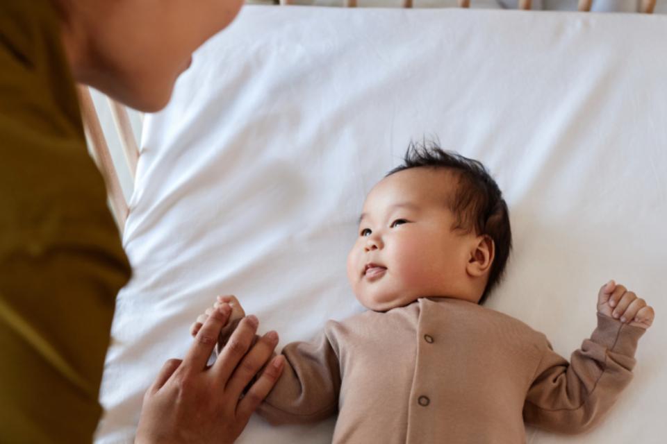 A baby is being put down to sleep in a cot. They are looking up at their parent.