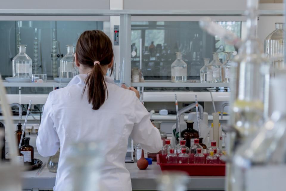 A researcher from the back, seemingly organising lab samples, wearing a lab coat with her hair tied back.