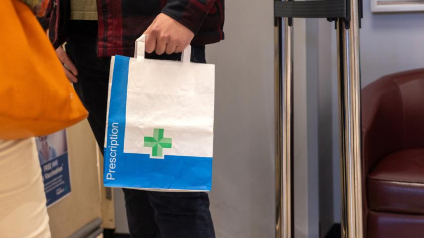 Someone's hand holding a paper pharmacy bag containing a prescription.
