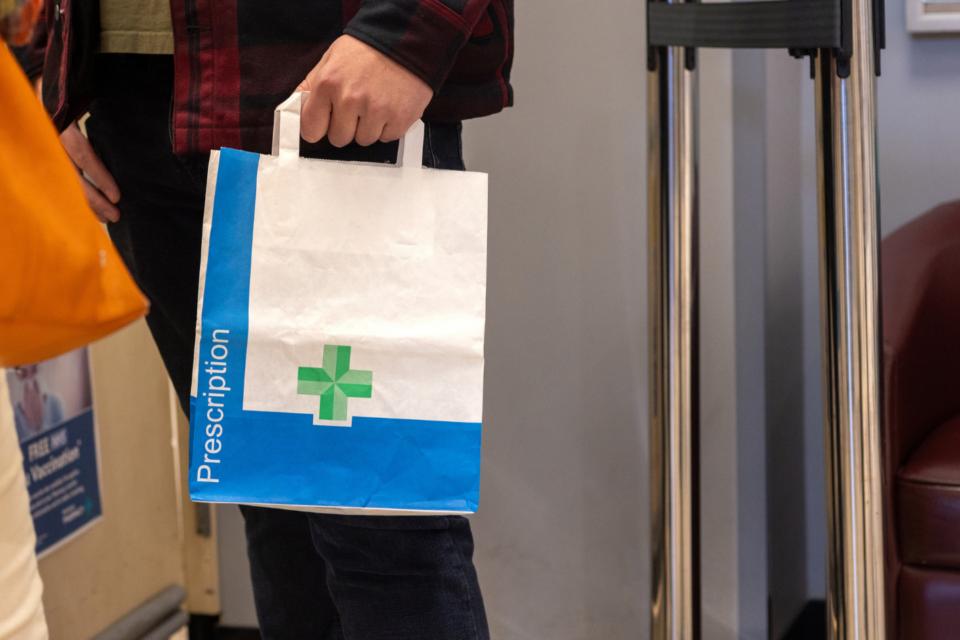 Someone's hand holding a paper pharmacy bag containing a prescription.