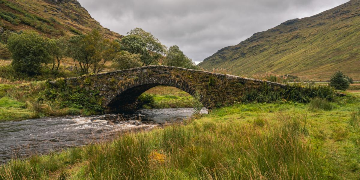 Bridge over a small lake, in front of mountains.