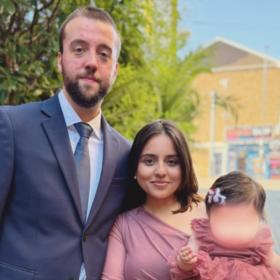 Murihah wearing a pink dress, next to her husband in a suit. She is holding Alannah