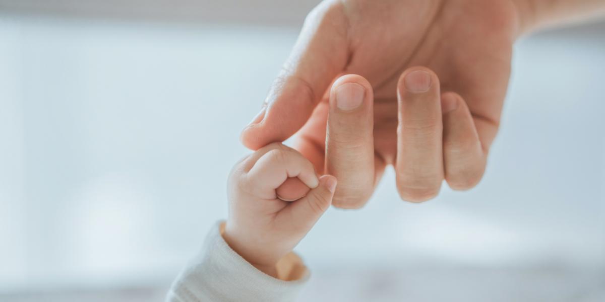 A baby's hand grasping their parent's index finger