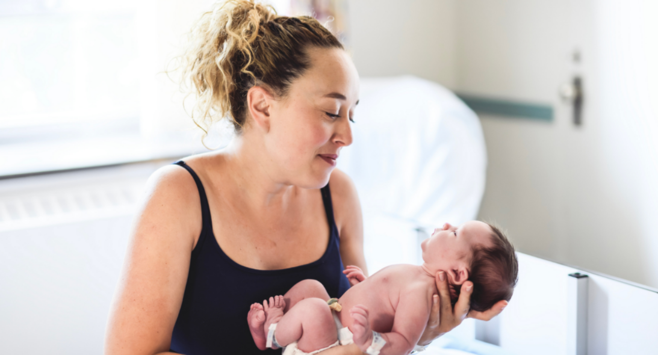 A mum is holding her young baby in her hands.