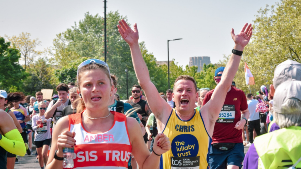 Marathon runner wearing Lullaby Trust vest cheering with his arms up in the air, running the race.
