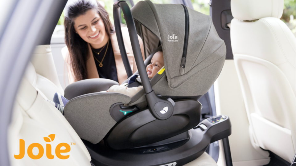 A young woman smiling at a baby in a carseat