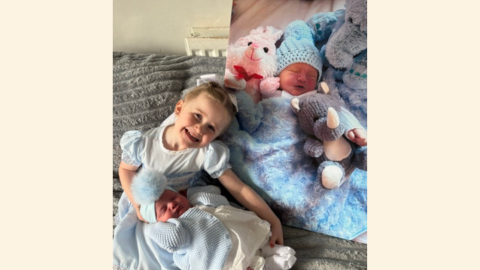 Roma smiling at the camera with Rosabella on her lap and a picture of Ralphie.