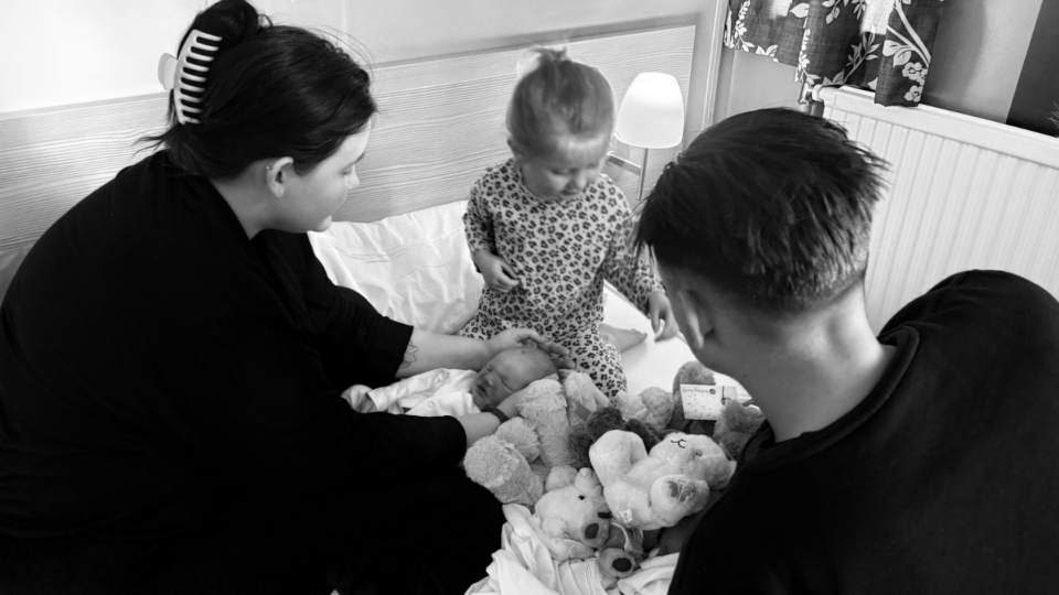 A black and white photo of Ruby stroking her little one's head, with Roma sitting beside her and Jacob's back to us.