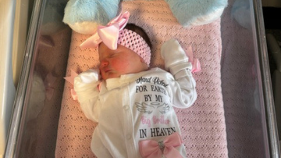 Rosabella sleeping on her back. She has a pink headband on and a white babygrow.