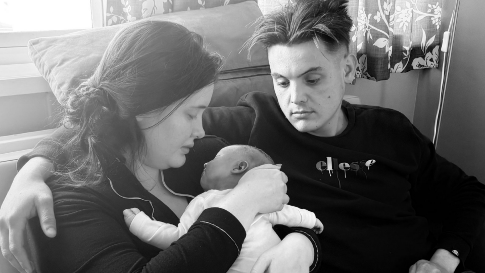 Ruby and Jacob holding their baby. They are looking a the baby lovingly. The photo is black and white