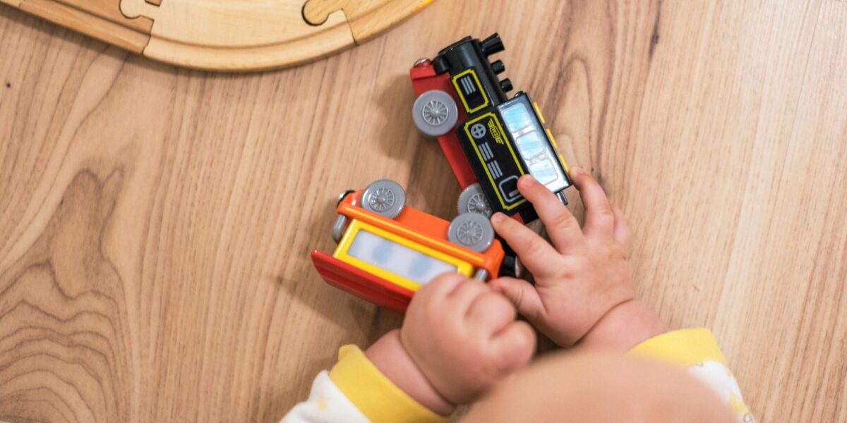 A close up of a baby's hands grasping at toy trains, near a wooden track.