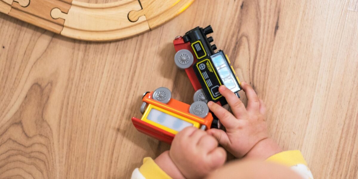 A close up of a baby's hands grasping at toy trains, near a wooden track.