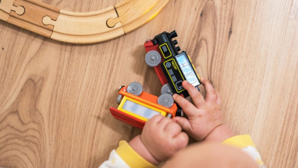 A close up of a baby's hands grasping at toy trains, near a wooden track.