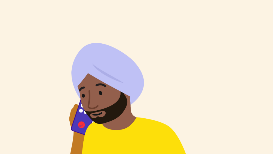 Man on phone wearing a yellow tshirt and wearing a turban, on a cream background.