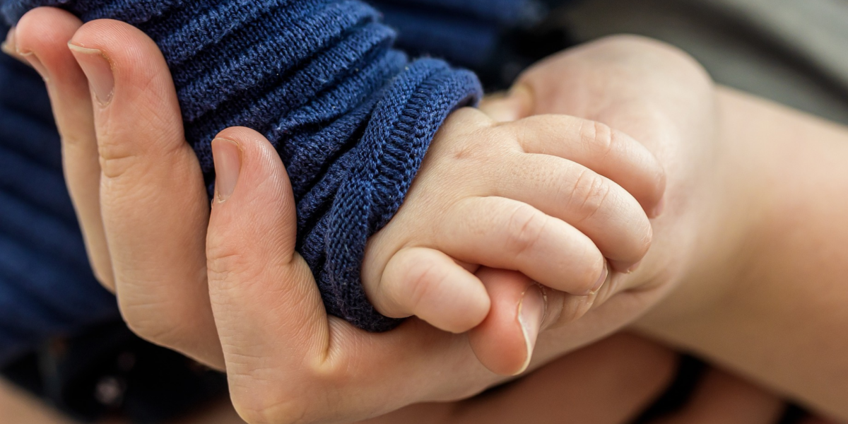 A close up of a baby's hand grasping the parent's hand