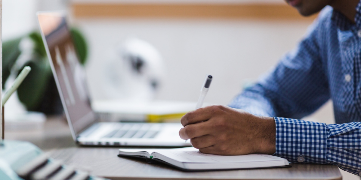 Close-up of a researcher making notes in a notebook. They have a laptop to the side of them.