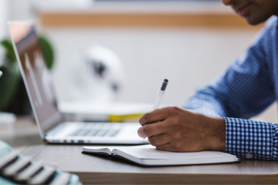 Close-up of a researcher making notes in a notebook. They have a laptop to the side of them.