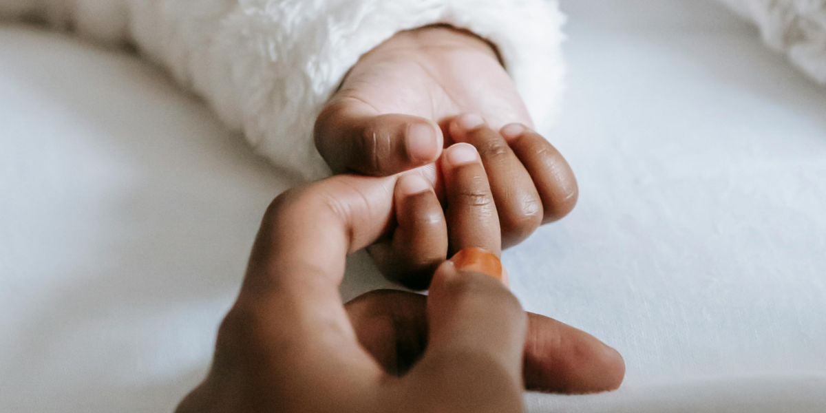 A baby's hand grasping their parent's index finger