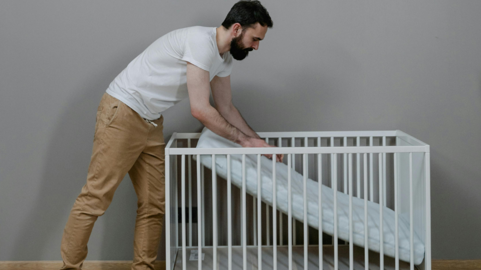 A parent is setting up the mattress in a cot. They are pushing the mattress onto the base of the cot.