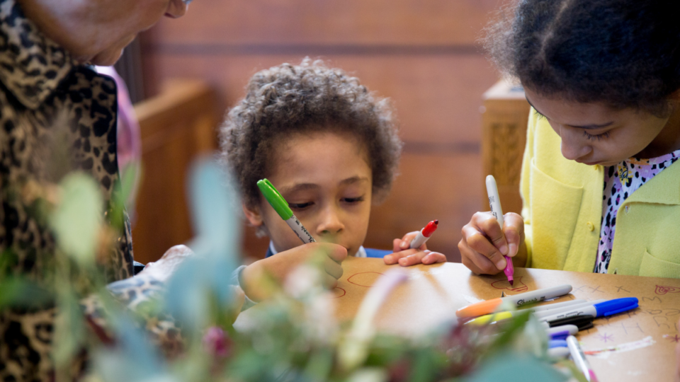 Children sitting at a table colouring in with pens.