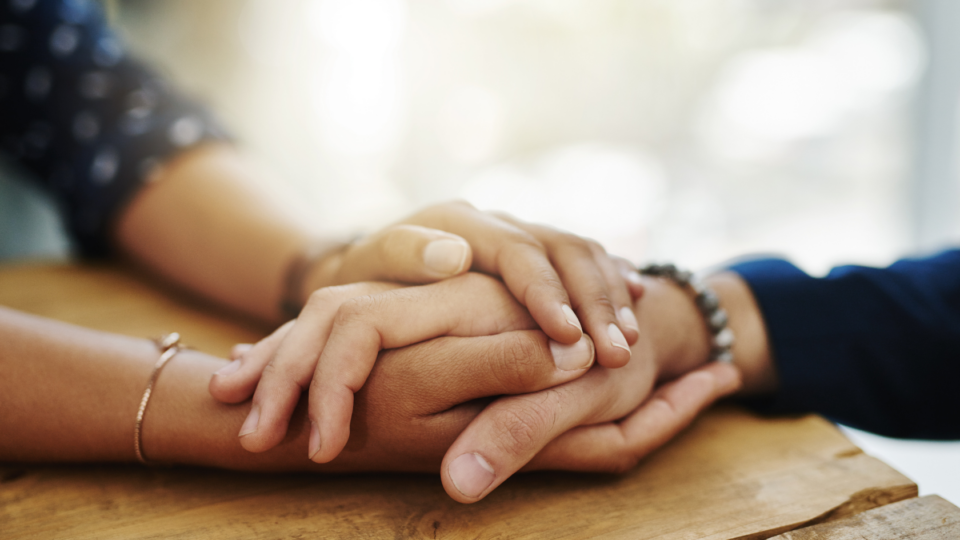 Two people holding hands with their hands resting on the table.