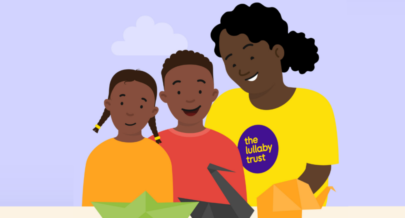 Illustration of a lady wearing a Lullaby Trust t-shirt standing beside two children who are smiling. On the table in front of them are some origami animals.