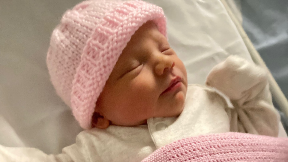 Baby Maisie wearing a pink hat and with a pink blanket.