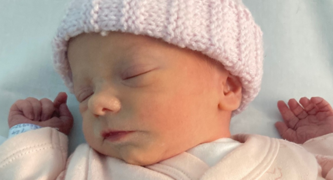 Baby Phoebe asleep, with a blue blanket and light pink hat.