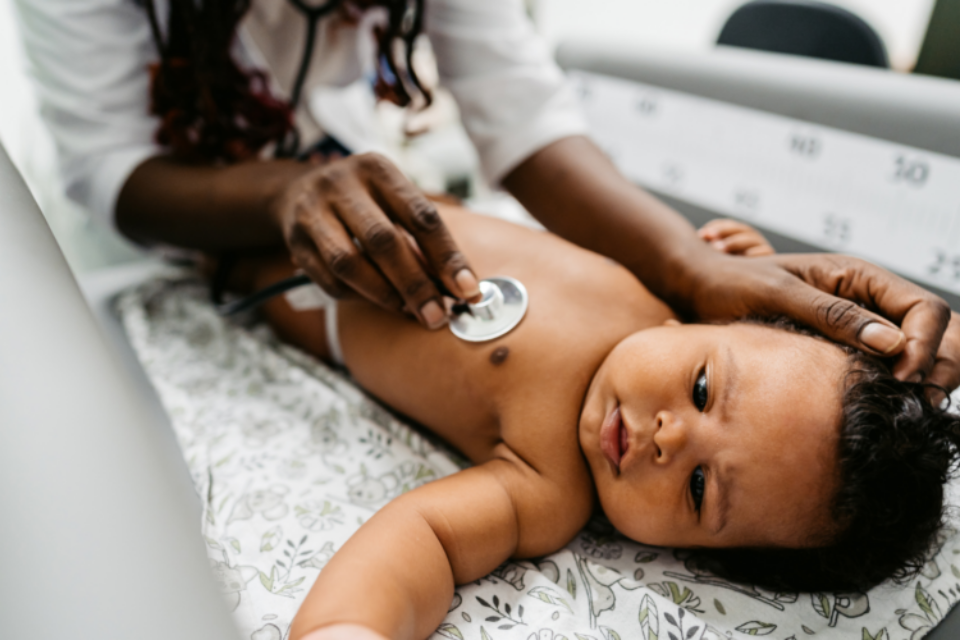 Baby lying on back as a doctor listens to their heart using a stethoscope.