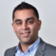 Photo of Amar wearing a blue shirt and grey suit jacket.