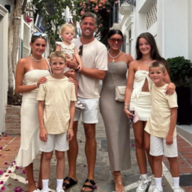 Matt holding his little girl, with his partner beside him and four other children. All wearing white on holiday.