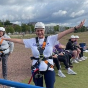 Margaret in a harness and a helmet with arms outstretched, about to do a bungee jump.
