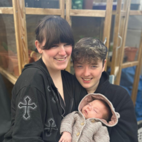 Lilly and James smiling at the camera, holding Theo.