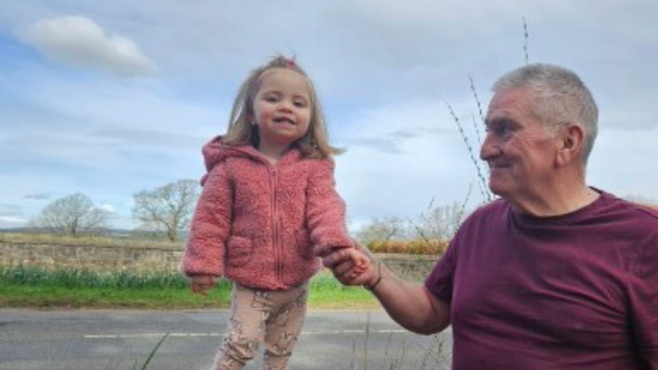 Barbara's partner smiling and holding their grandaughter's hand who is wearing a pink coat.