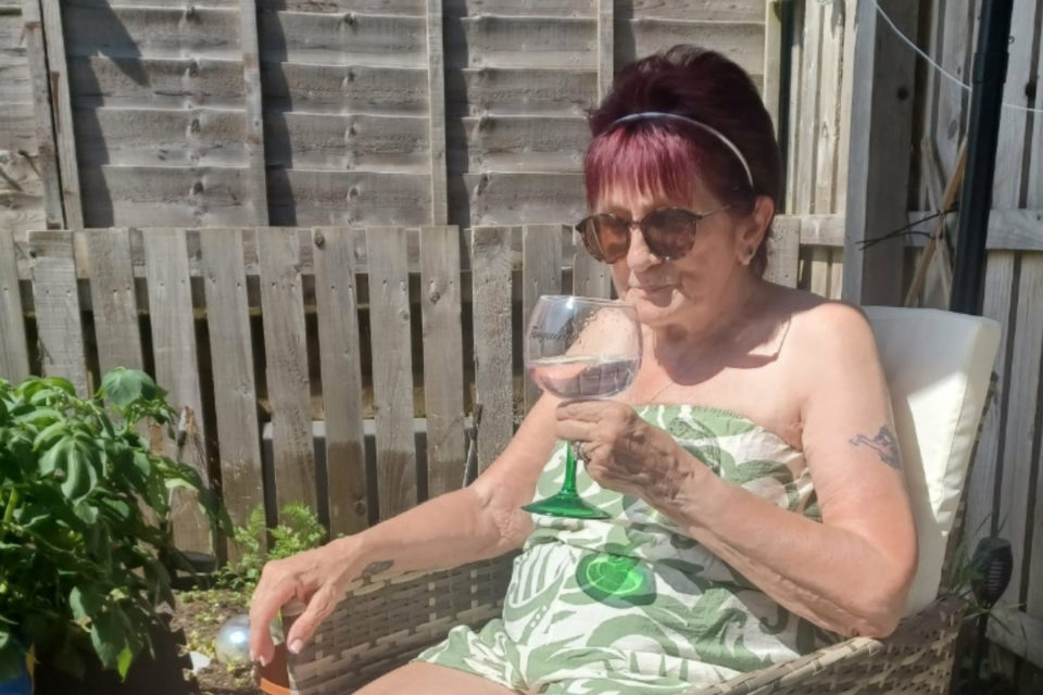 Barbara sitting on a chair in the sun holding a glass of drink,