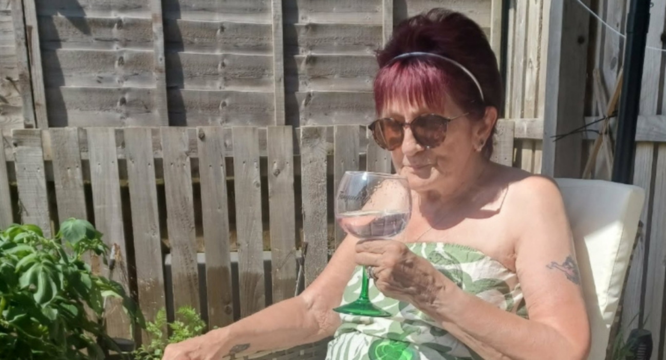 Barbara sitting on a chair in the sun holding a glass of drink,