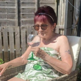 Barbara sitting on a chair in the sun holding a glass of drink,