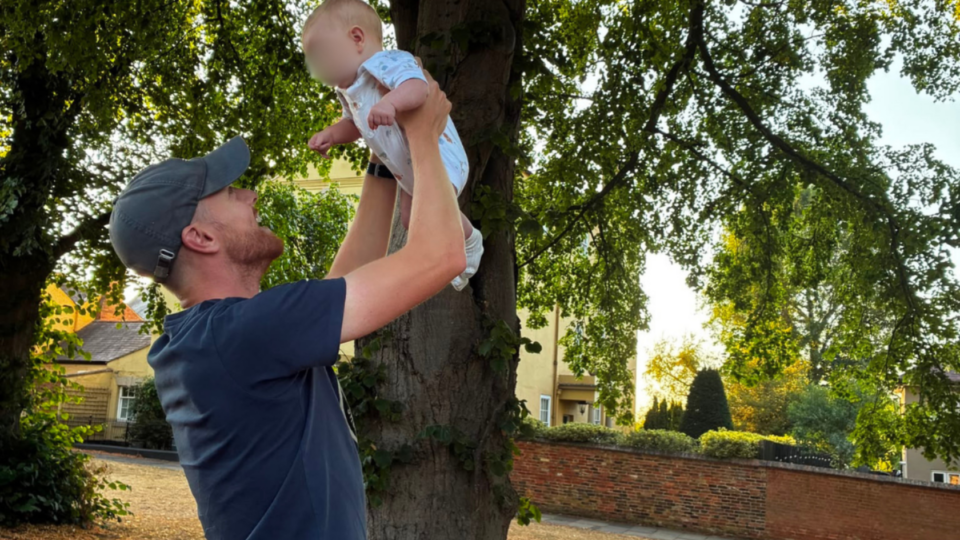 Alex and Oakley in Southwell. Alex is holding Oakley up in the sky, smiling