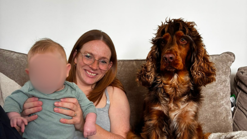 Paige holding Oakley with the dog sat next to her on the sofa.