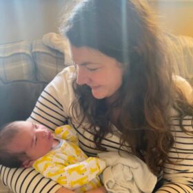Beth holding Joshua, wearing a stripy top sitting on the sofa