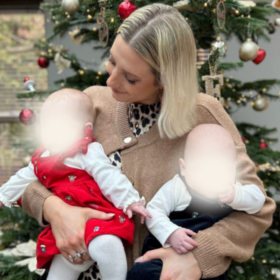 Jess holding her twins and standing in front of a Christmas tree.