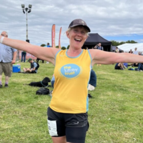 Clare wearing a Lullaby Trust t-shirt, ready for a run with her arms spread wide and smiling.