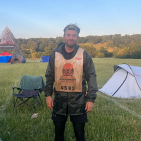 Stefan wearing a head torch and a vest, with a tent in the background.