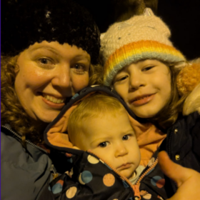 Lucy and her children in coats and wooly hats, smiling at the camera.