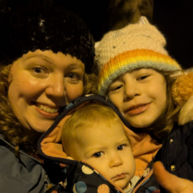 Lucy and her children in coats and wooly hats, smiling at the camera.