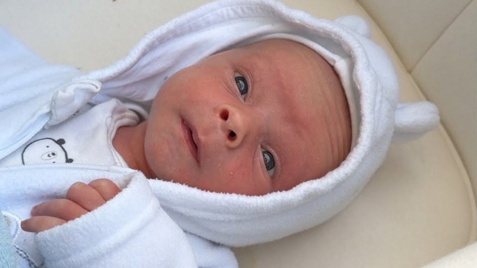 Samuel in a white babygrow with the hood up, looking up with his big eyes.