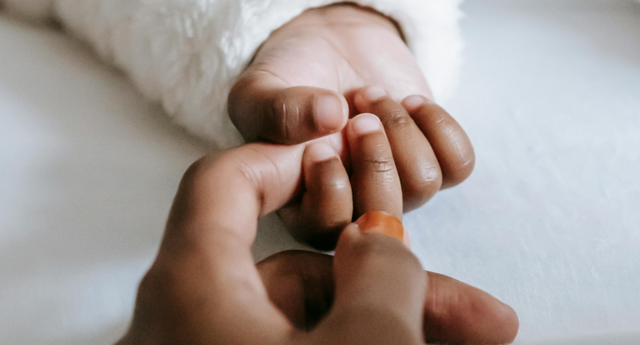 A baby's hand grasping their parent's index finger
